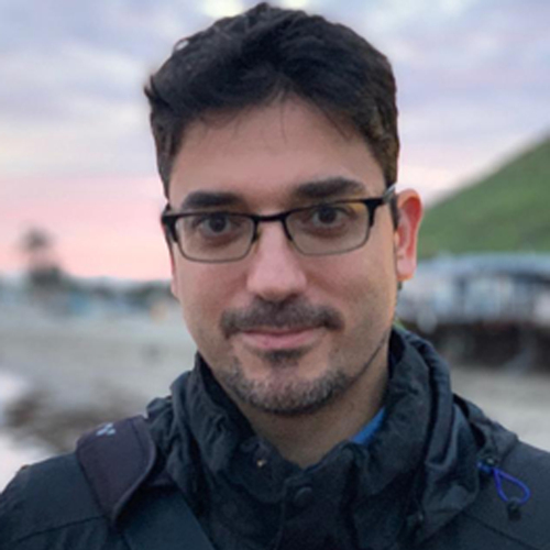 A one-quarter-length portrait photograph of art historian and classicist Jesús Muñoz Morcillo, age mid-40s, looking friendly at the viewer in a bright, outdoor setting. He has short black hair and wears glasses.
